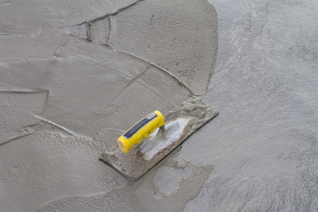 Yellow-handled trowel spreads wet cement across a flat concrete surface during patio construction.
