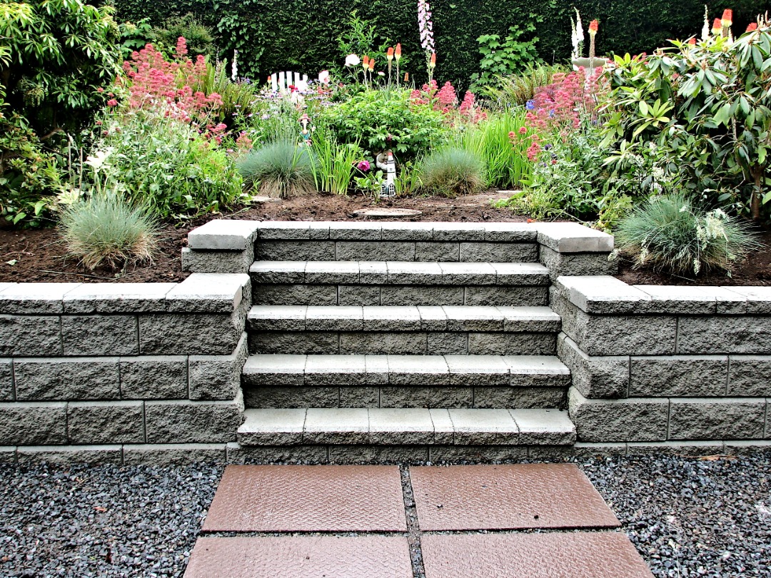 A symmetrical set of stone steps leading up to a vibrant garden, framed by retaining walls with neatly arranged flowers and shrubs.