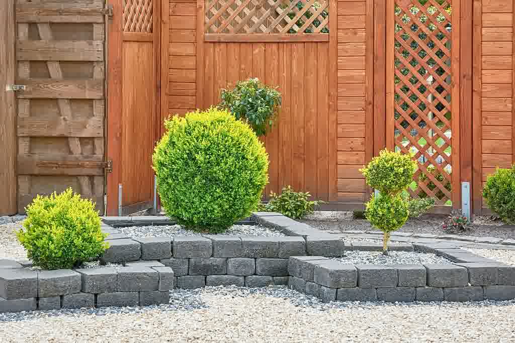 A dark stone retaining wall with vibrant bushes.