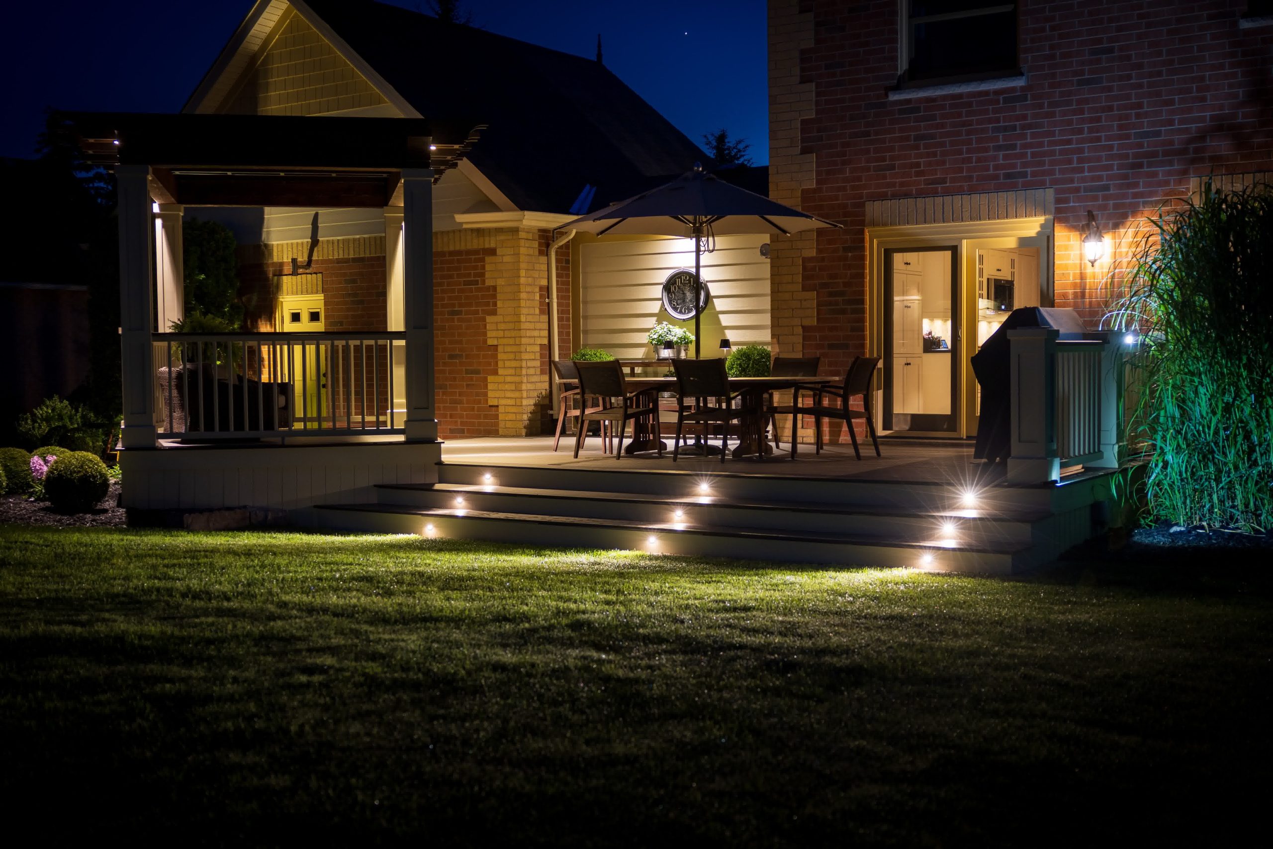 Cozy backyard patio with built-in lighting, dining area, gazebo, and landscaped lawn, illuminated at night for warm ambiance.